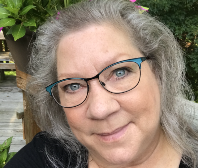 Michelle smiling at the camera as she wears glasses and has gray hair.